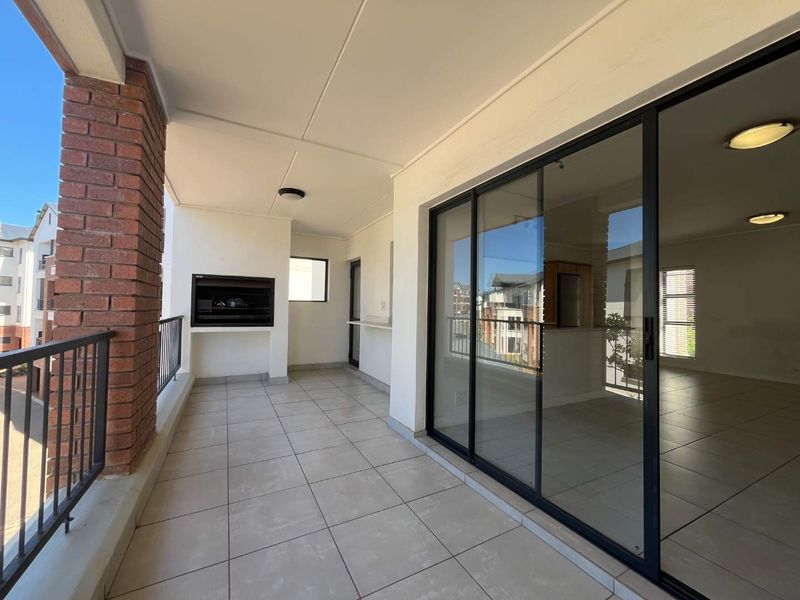 Spacious covered balcony featuring a built-in braai, tiled flooring, and large sliding glass doors providing seamless access to the interior living area.