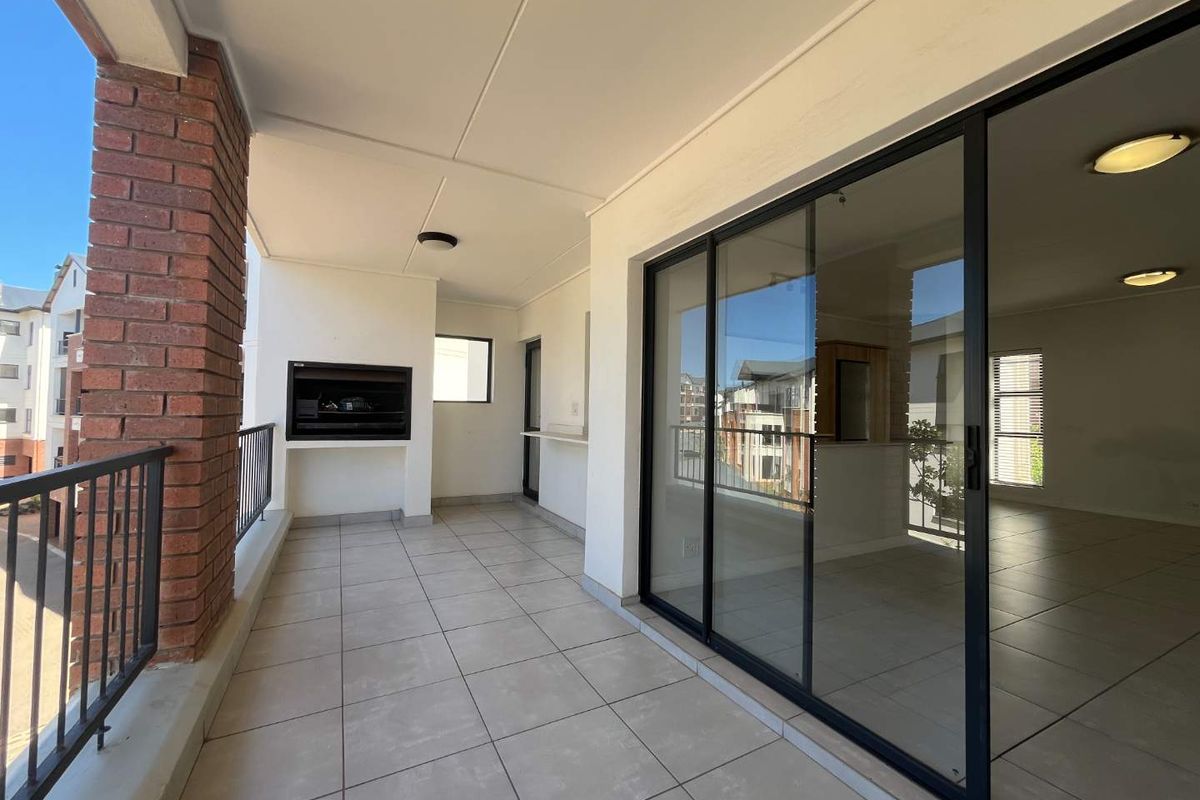 Spacious covered balcony featuring a built-in braai, tiled flooring, and large sliding glass doors providing seamless access to the interior living area.