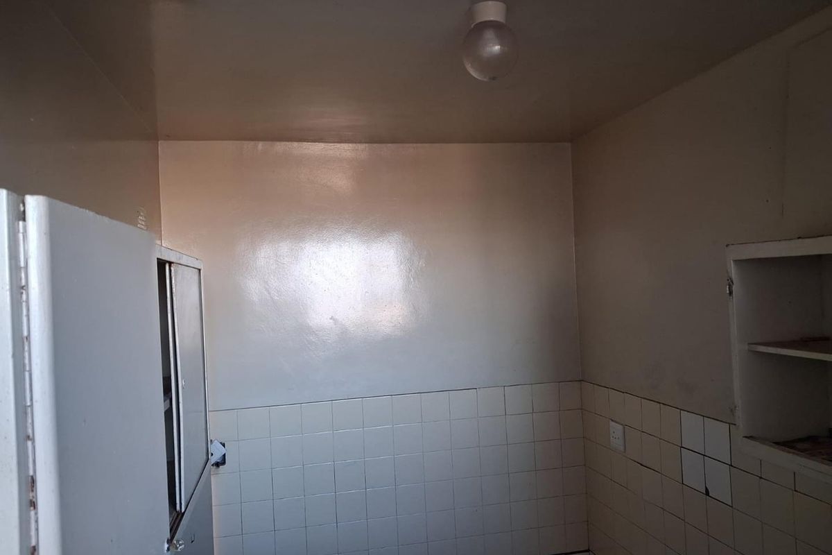 A compact, empty kitchen area featuring tiled splashbacks, built-in shelving, and basic cabinetry, requiring cosmetic updates to modernize the space.