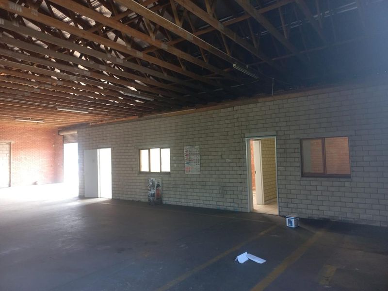 Spacious industrial utility area featuring exposed timber roof trusses, concrete flooring, and cinder block walls, suitable for workshop or storage use.