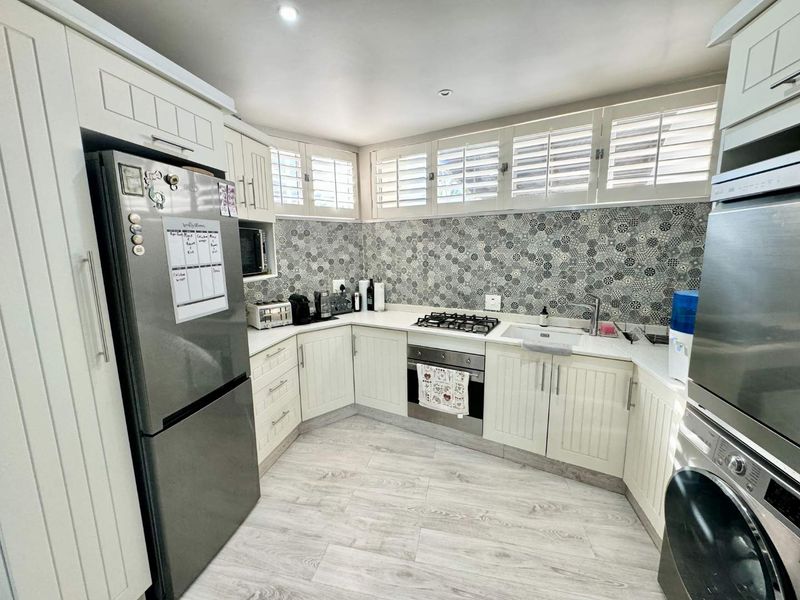 A well-maintained kitchen featuring white cabinetry, a patterned tiled backsplash, gas hob, built-in oven, and plantation shutters for natural light control.