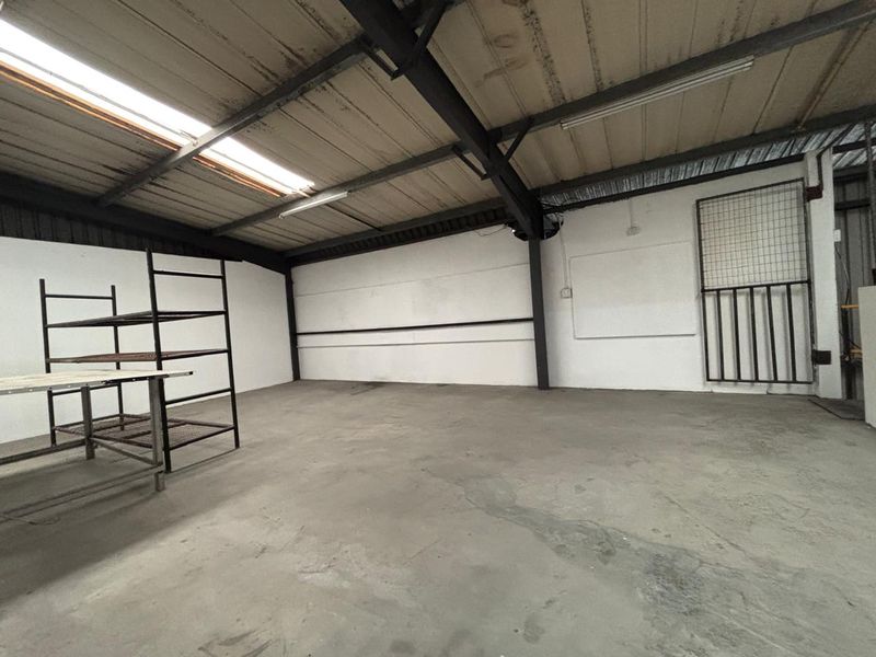 Spacious industrial utility area featuring exposed steel beams, corrugated roofing with skylights, and durable concrete flooring, suitable for storage or workshop use.
