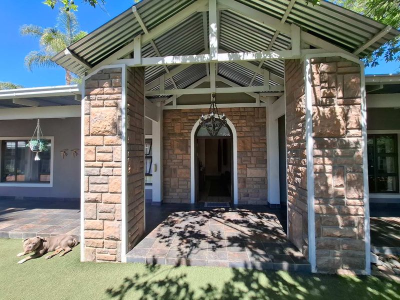 A welcoming front entrance featuring stone-clad pillars, a covered tiled patio, and a distinctive arched doorway under a corrugated metal roof.