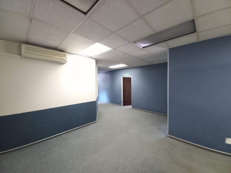 A spacious office hallway featuring a suspended acoustic ceiling, wall-mounted air conditioning unit, and blue accent walls.