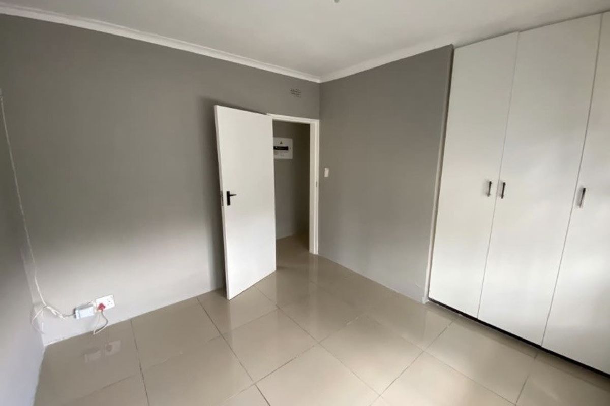A clean, empty bedroom featuring neutral grey walls, large format floor tiles, and white built-in cupboards with modern hardware.