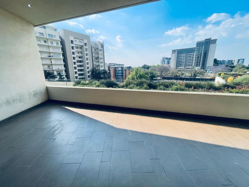 Spacious covered balcony featuring modern tiled flooring and a sleek glass balustrade, offering expansive urban views.