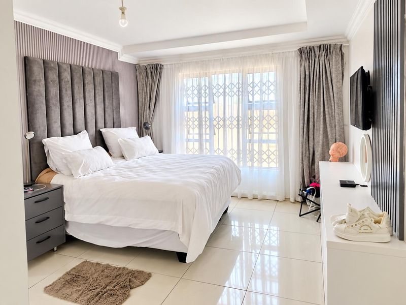 A well-maintained bedroom featuring tiled flooring, a recessed ceiling, and a large window fitted with a security gate.