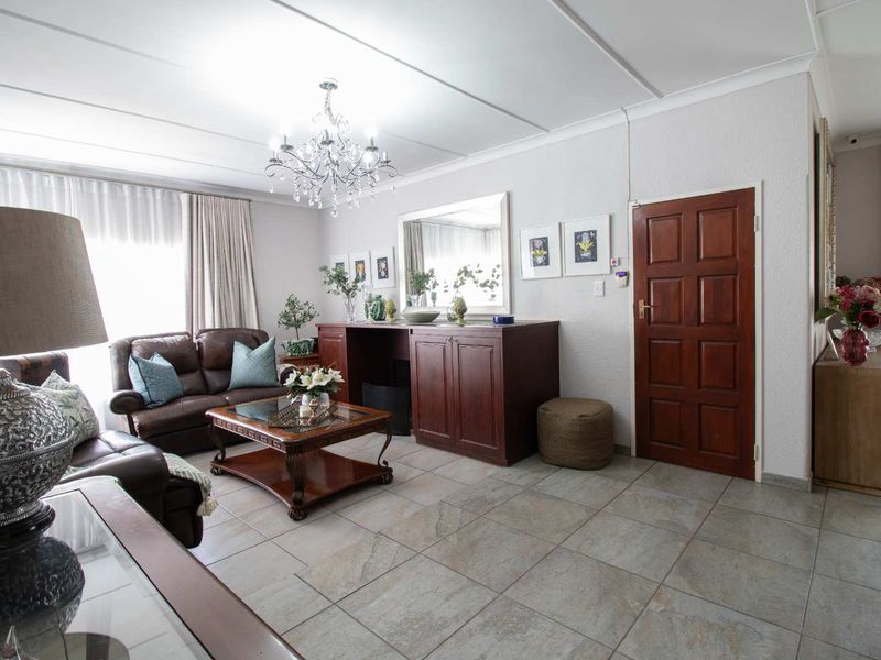 A well-maintained living room featuring neutral tiled flooring, a decorative crystal chandelier, and built-in wooden cabinetry, offering a classic and comfortable living space.
