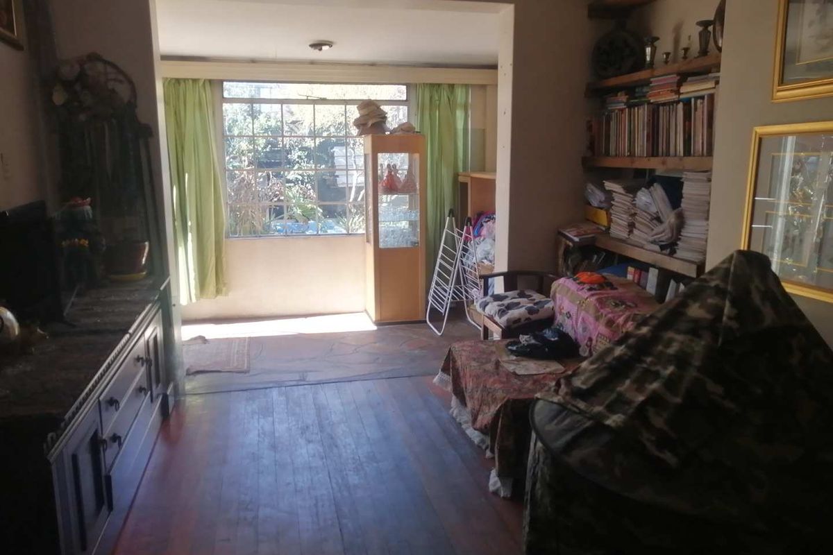 A living room featuring timber flooring, built-in wooden shelving, and a large window providing natural light and a view of the garden.