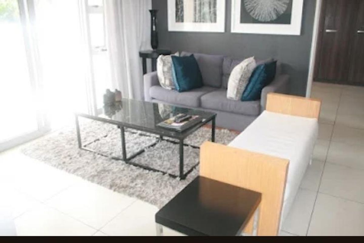 A bright living room featuring large sliding glass doors, neutral floor tiles, and a modern dark accent wall.