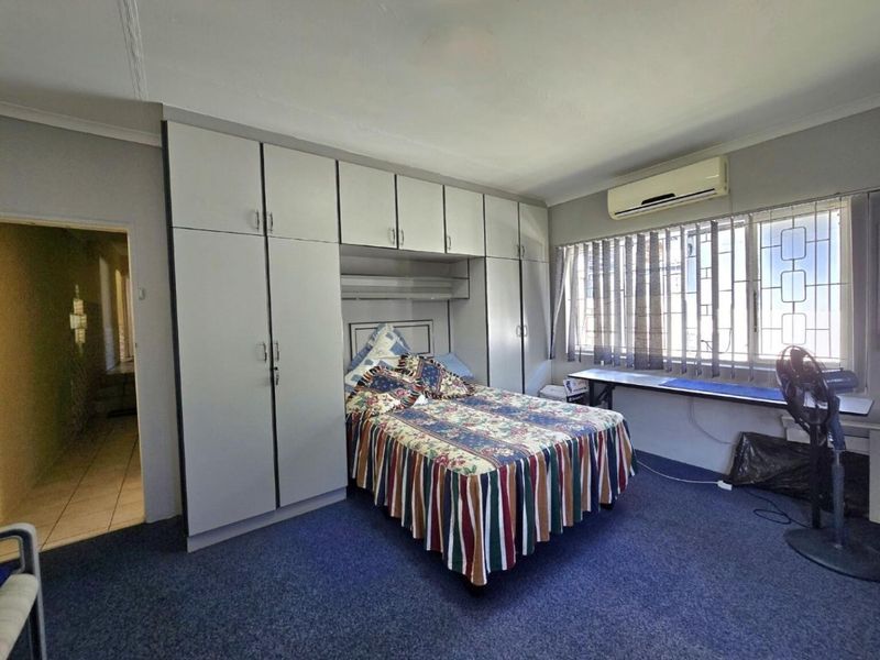 A bedroom featuring extensive built-in cabinetry, a wall-mounted air conditioning unit, and a fitted desk area with security bars on the windows.