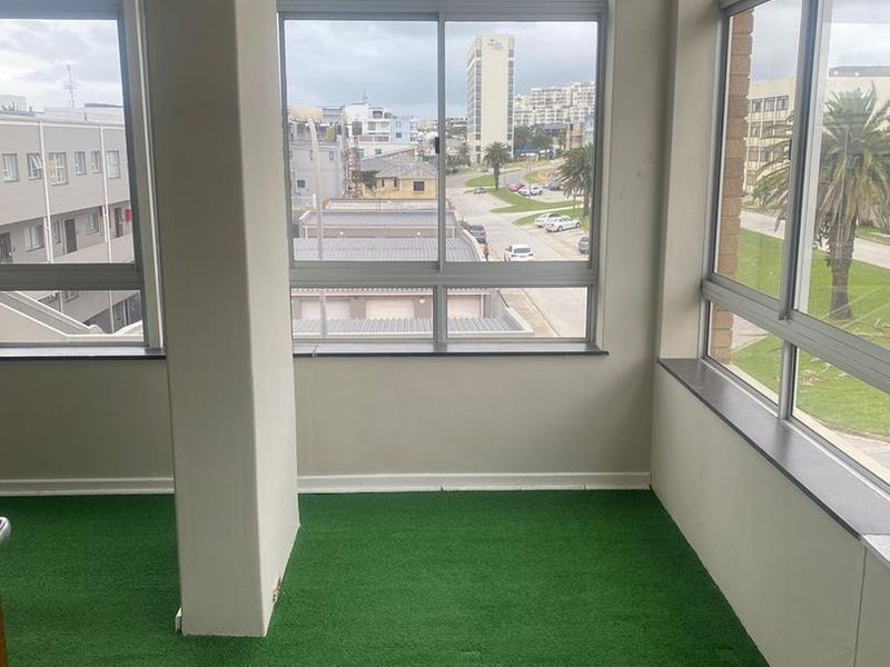 Enclosed balcony area featuring large aluminium sliding windows, artificial grass flooring, and an urban neighbourhood view.