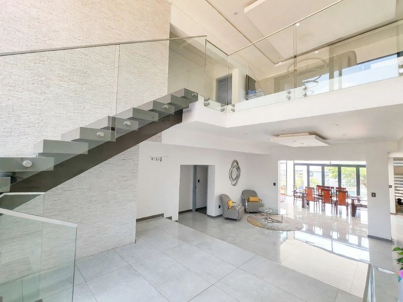 Spacious open-plan living area featuring a modern floating staircase with glass balustrades, double volume ceilings, and high-quality porcelain floor tiles.