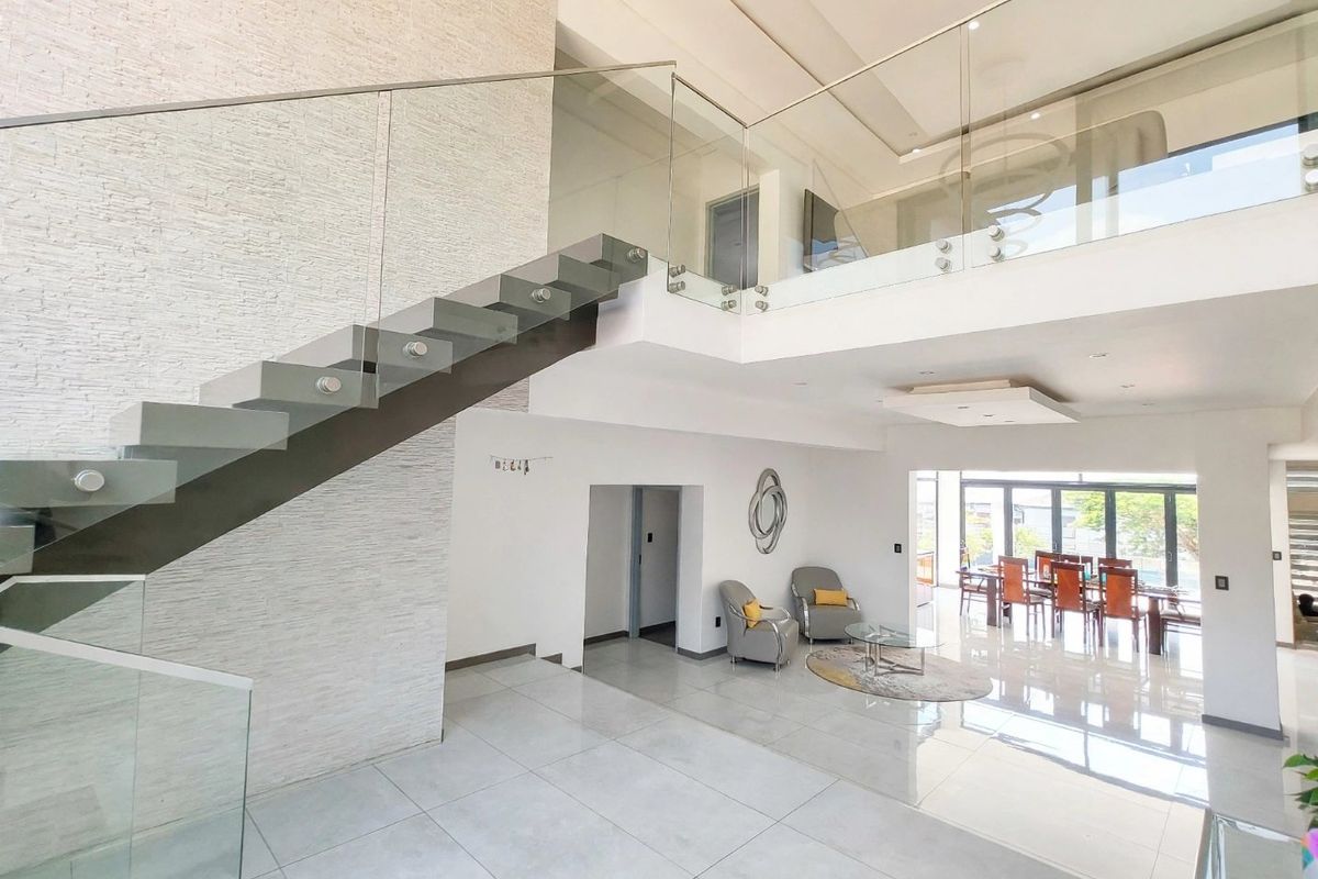 Spacious open-plan living area featuring a modern floating staircase with glass balustrades, double volume ceilings, and high-quality porcelain floor tiles.
