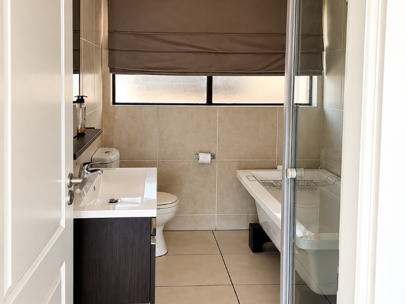 A well-maintained bathroom featuring a modern vanity, toilet, freestanding bathtub, and a separate glass-enclosed shower with neutral floor-to-ceiling tiling.
