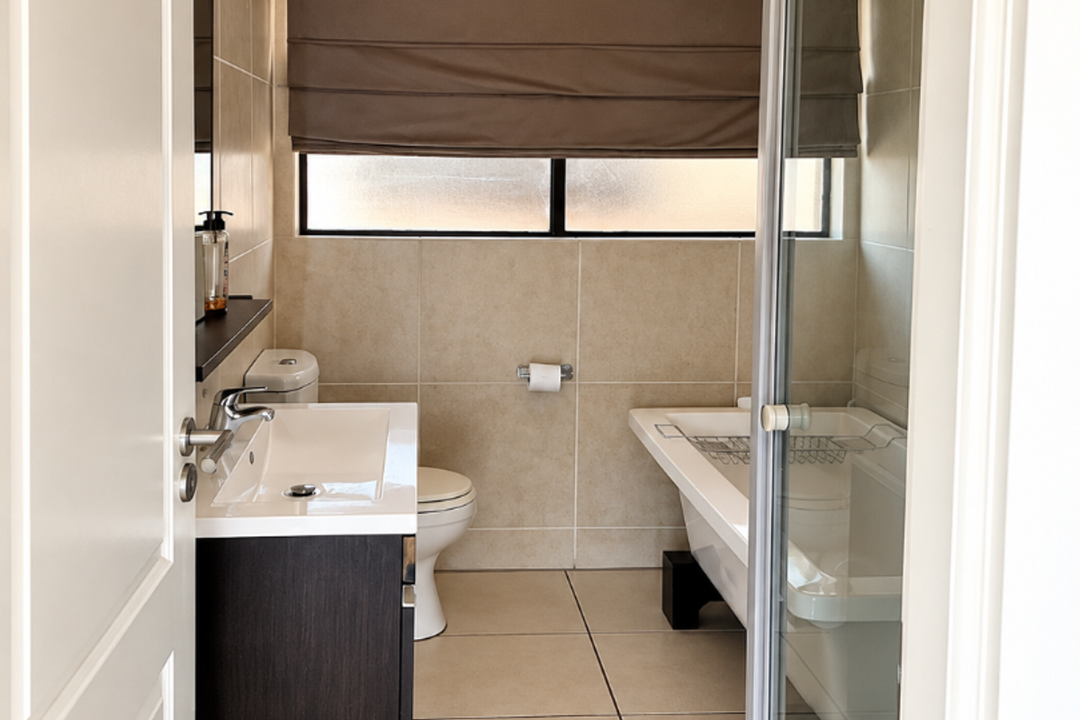 A well-maintained bathroom featuring a modern vanity, toilet, freestanding bathtub, and a separate glass-enclosed shower with neutral floor-to-ceiling tiling.