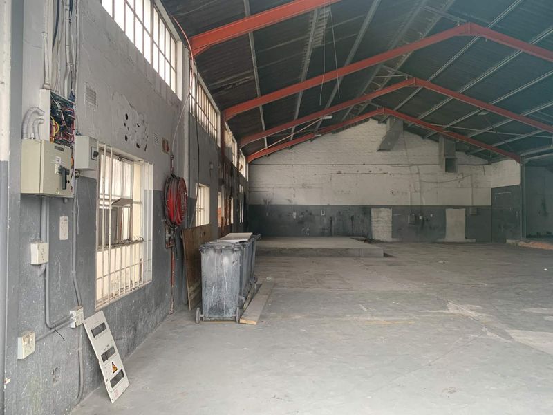Spacious industrial utility space featuring exposed steel roof trusses, concrete flooring, and functional electrical infrastructure, suitable for warehouse or workshop use.