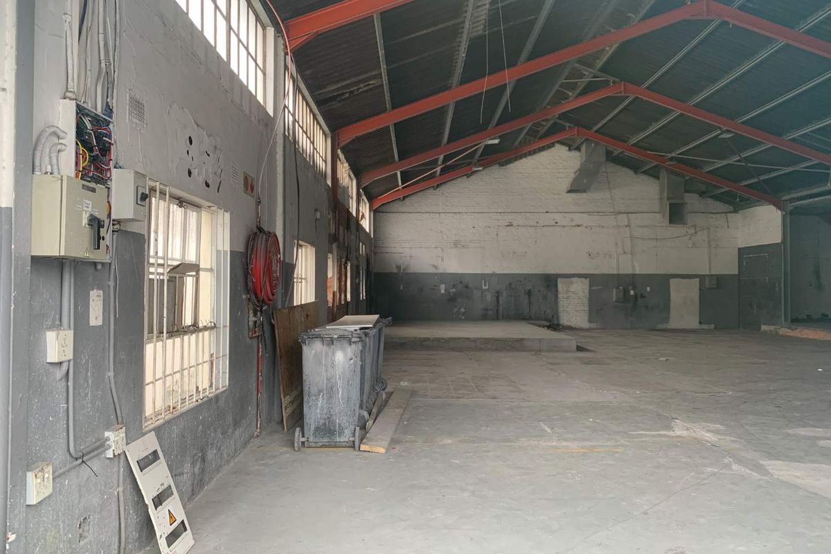 Spacious industrial utility space featuring exposed steel roof trusses, concrete flooring, and functional electrical infrastructure, suitable for warehouse or workshop use.