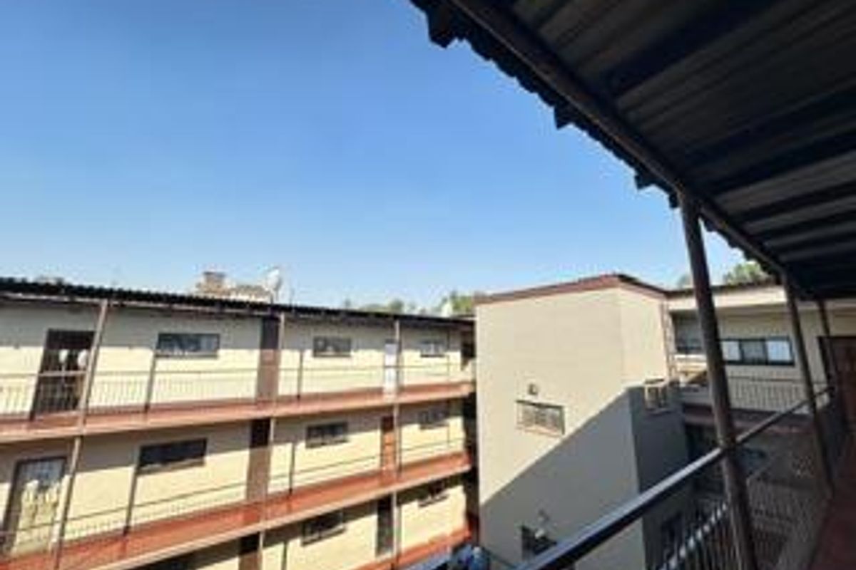 View of the apartment complex exterior, featuring multi-level walkways, metal railings, and a corrugated roof structure.