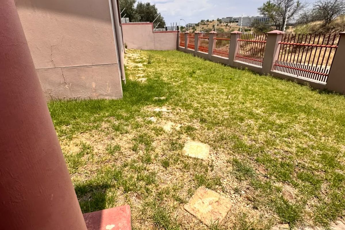 Rear garden area featuring a stone-paved patio, lawn with stepping stones, and metal perimeter fencing along the property boundary.