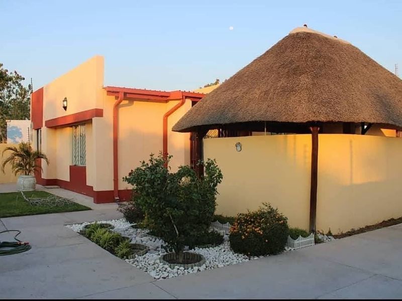 Front view of a residential property featuring a distinctive thatched roof structure, concrete driveway, and landscaped garden beds.