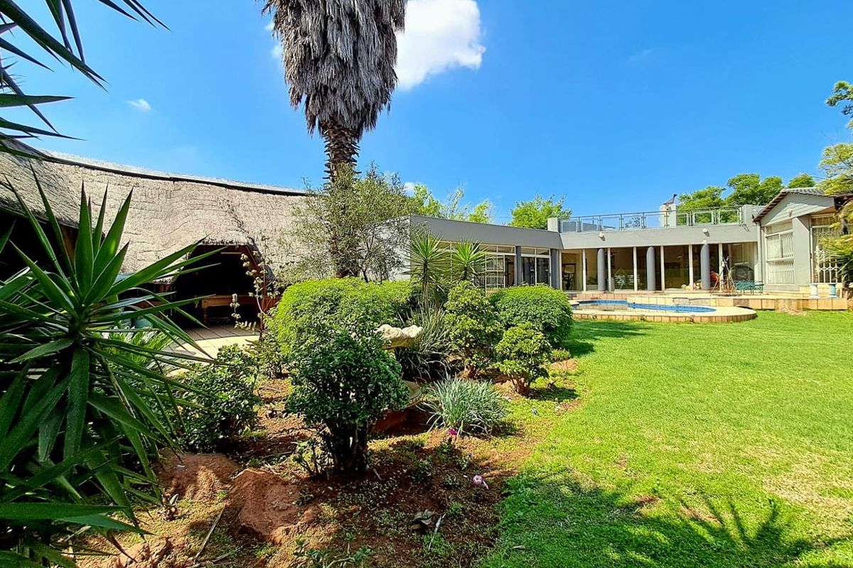 Spacious rear garden featuring a swimming pool, a thatched entertainment area, and a balcony overlooking the landscaped outdoor space.