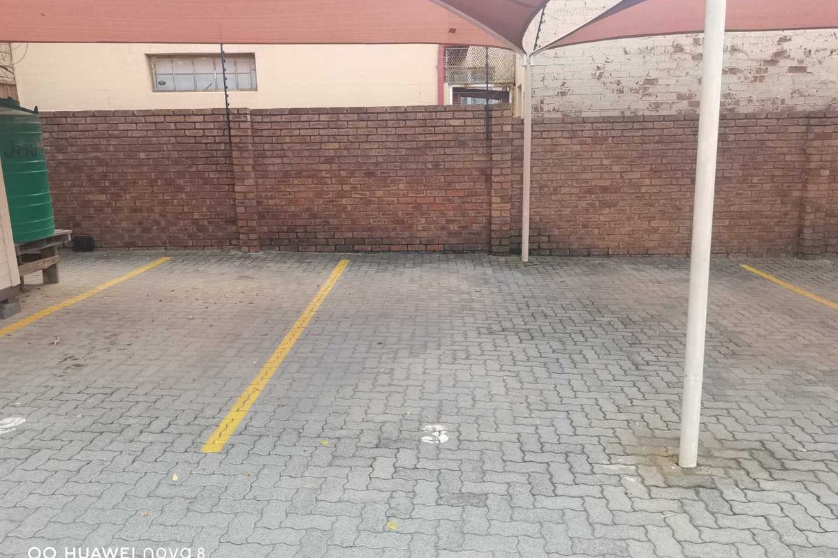 Covered parking area featuring paved bays, a brick boundary wall, and a shade sail structure.
