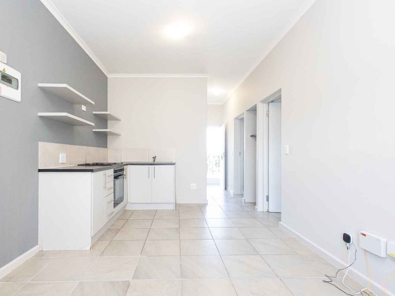An open-plan kitchen and living area featuring modern white cabinetry, built-in oven, hob, and neutral tiled flooring in a clean, well-maintained space.