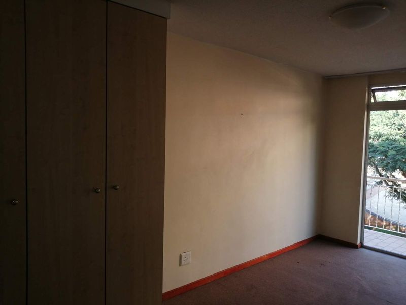 An empty bedroom featuring built-in cupboards, carpeted flooring, and a sliding glass door providing access to an outdoor balcony area.