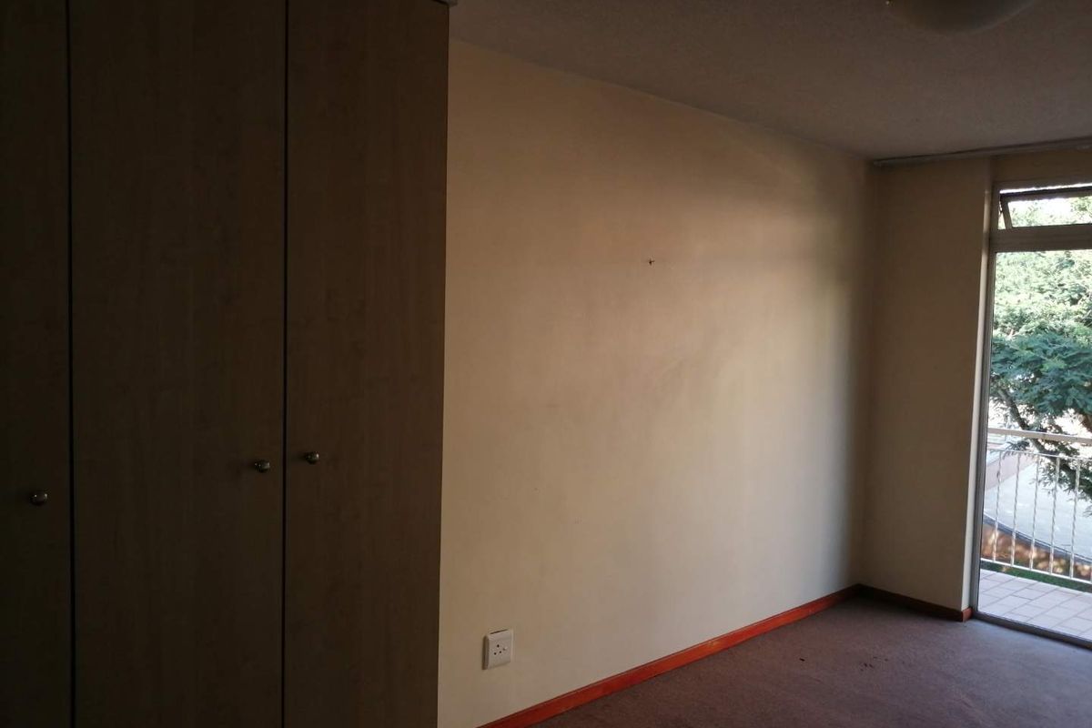 An empty bedroom featuring built-in cupboards, carpeted flooring, and a sliding glass door providing access to an outdoor balcony area.