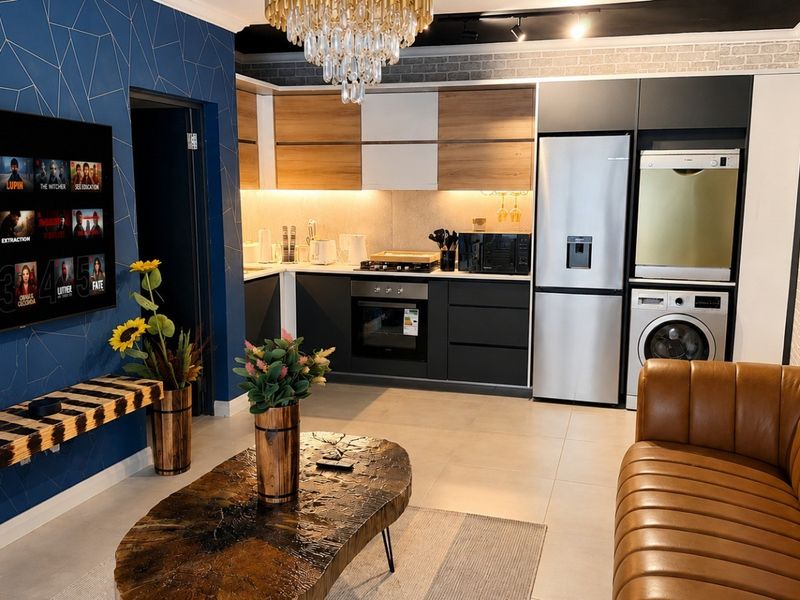 Modern open-plan living area featuring a contemporary kitchen with built-in cabinetry, integrated appliances, and a stylish brick feature wall.