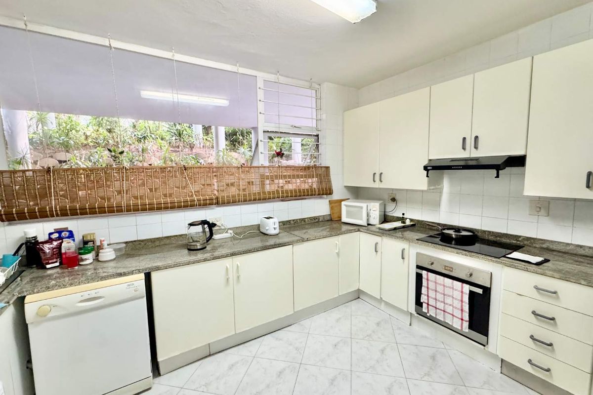 A functional kitchen featuring white cabinetry, granite countertops, a built-in oven, hob, and extractor fan, with large windows providing natural light.