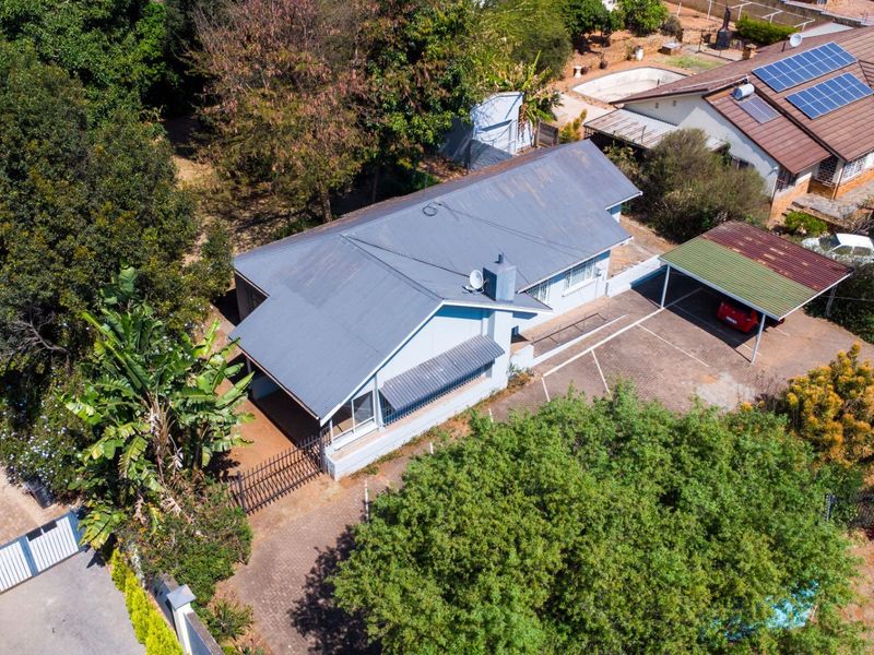 Aerial view of the property featuring a metal roof, paved driveway, and a covered carport, set within a landscaped residential plot.
