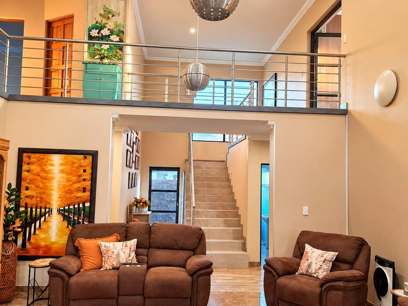 Spacious double-volume living area featuring a mezzanine level with stainless steel balustrades and a tiled staircase leading to the upper floor.