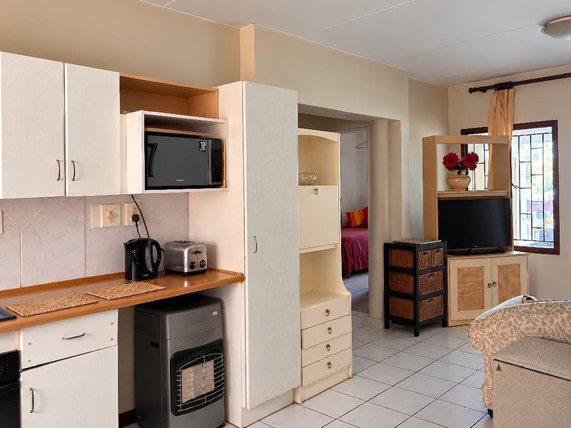 Open-plan living area featuring a functional kitchen with built-in cabinetry, oven, and hob, seamlessly flowing into the adjacent living space with tiled flooring throughout.
