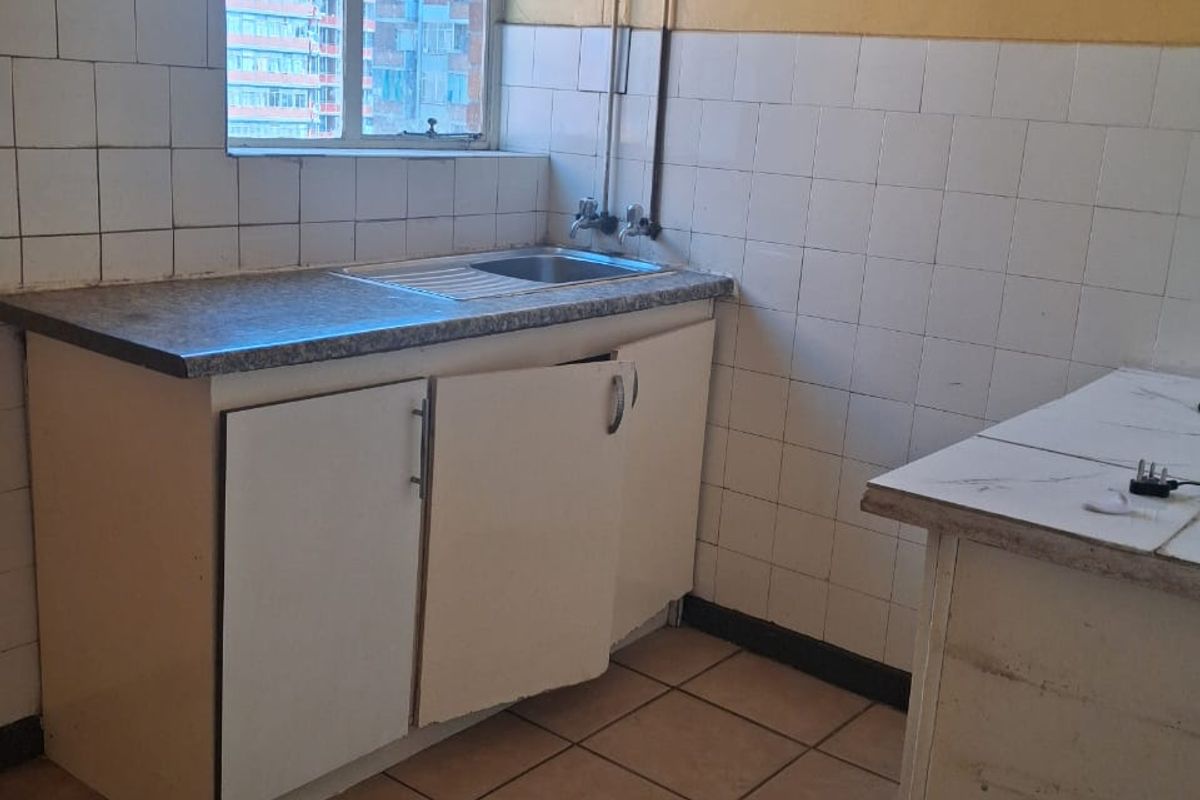 A dated kitchen area featuring tiled walls, a stainless steel sink, and built-in cabinetry in need of repair and modernization.