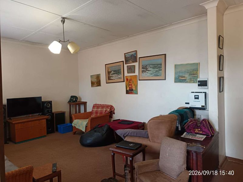 A living room featuring a wall-mounted solar inverter and electrical distribution board, with standard ceiling tiles and coving.