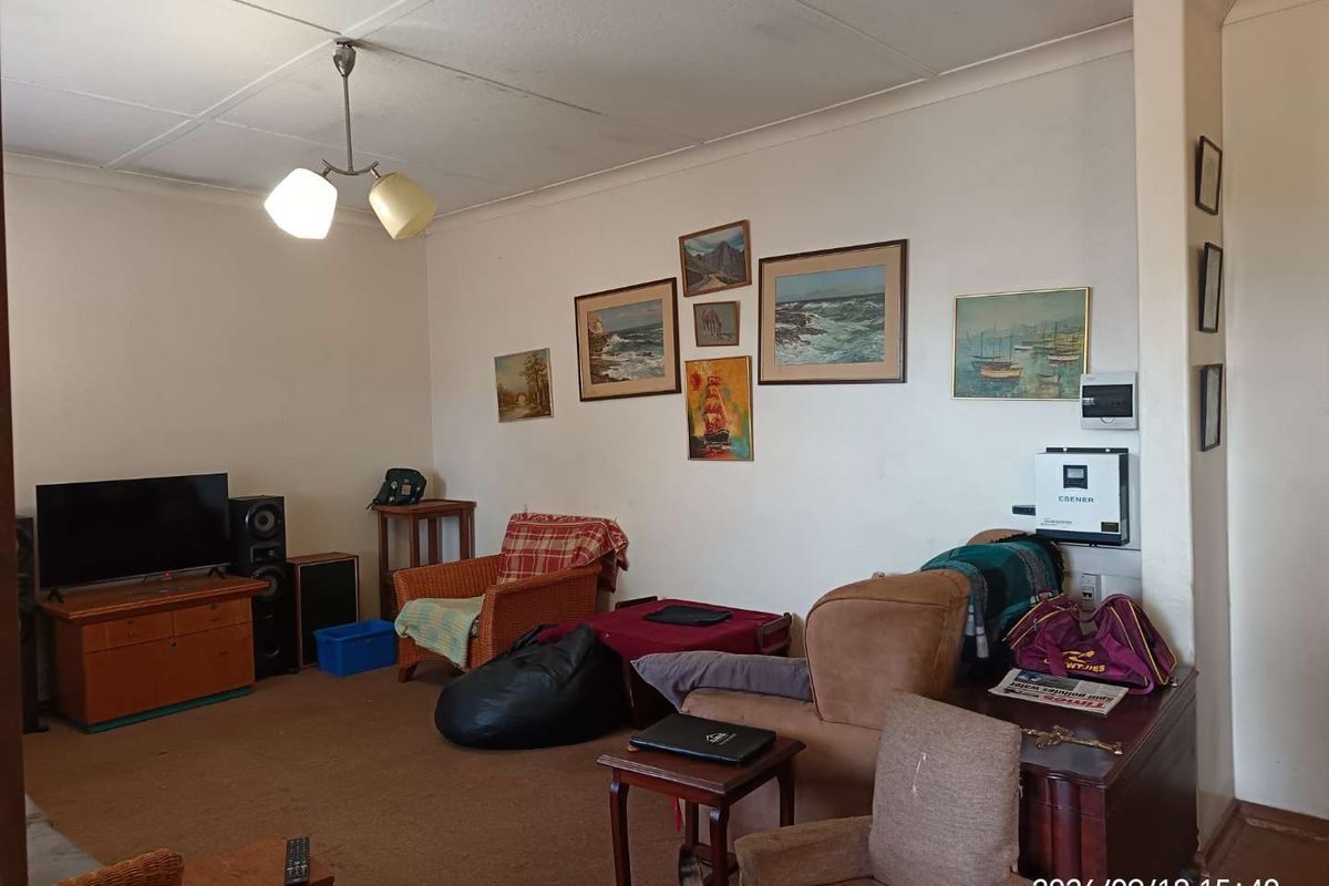 A living room featuring a wall-mounted solar inverter and electrical distribution board, with standard ceiling tiles and coving.