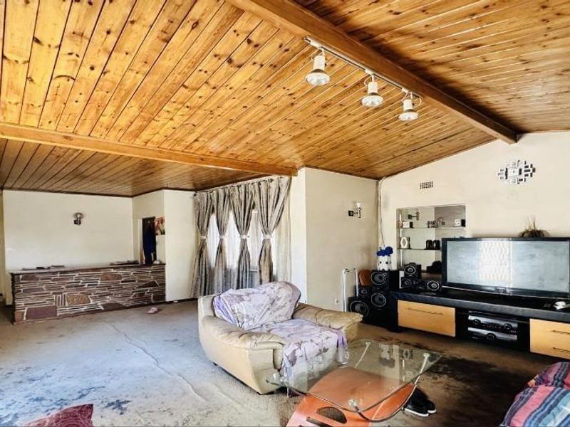 Spacious living room featuring a distinctive timber-clad ceiling, track lighting, and a built-in stone-clad bar counter.