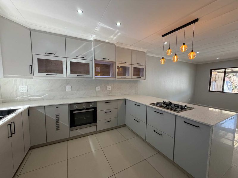 Modern kitchen featuring sleek grey cabinetry, stone countertops, built-in oven, gas hob, and stylish pendant lighting, offering a clean and contemporary culinary space.