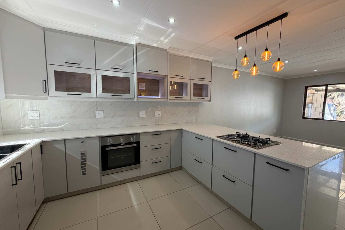 Modern kitchen featuring sleek grey cabinetry, stone countertops, built-in oven, gas hob, and stylish pendant lighting, offering a clean and contemporary culinary space.