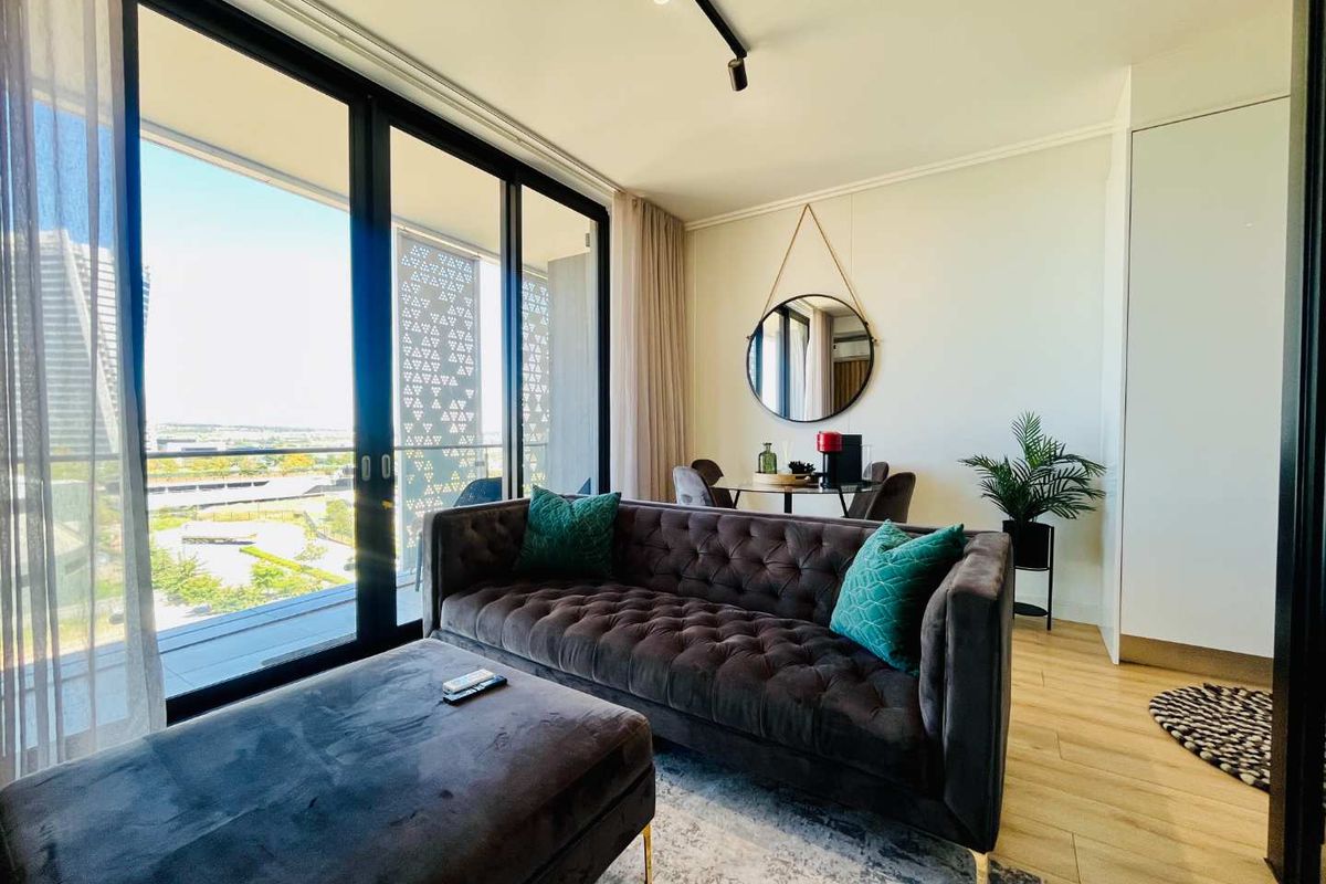 Modern living room featuring sleek laminate flooring, track lighting, and large sliding glass doors that open to a balcony with expansive views.