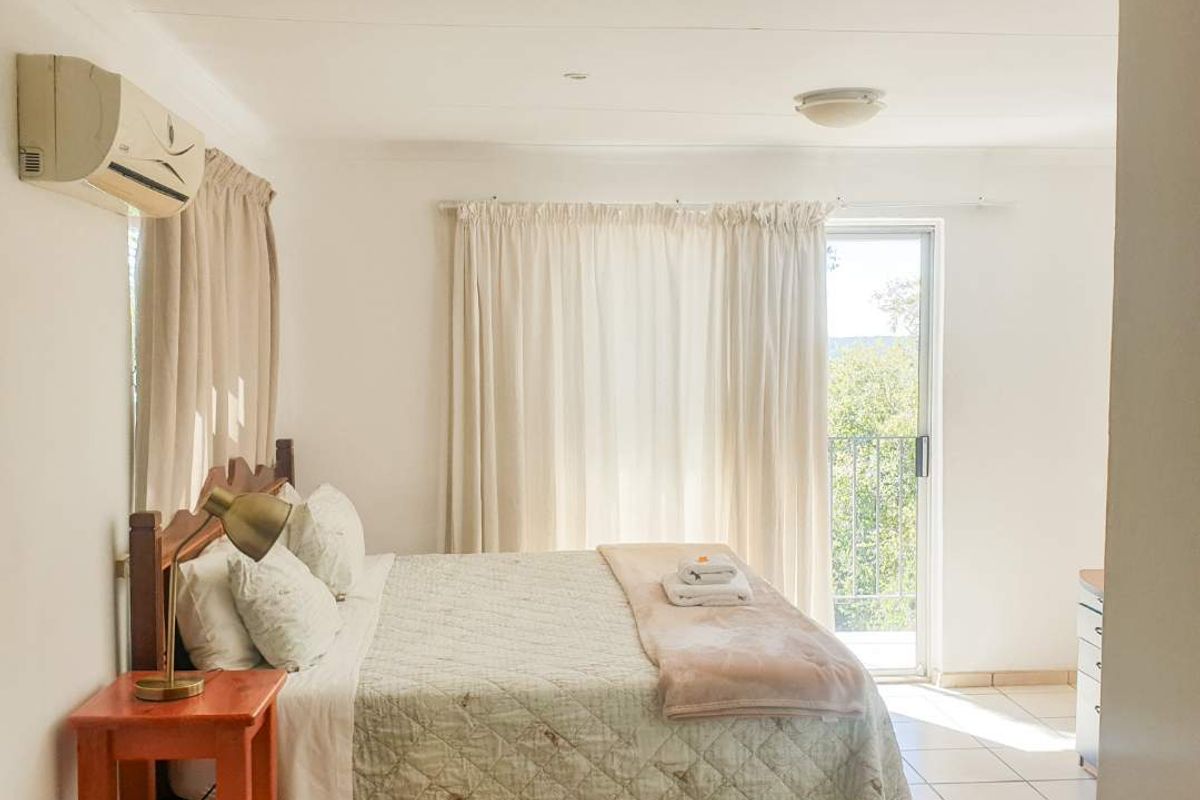 A bright bedroom featuring tiled flooring, a wall-mounted air conditioning unit, and direct access to a private balcony through a sliding glass door.
