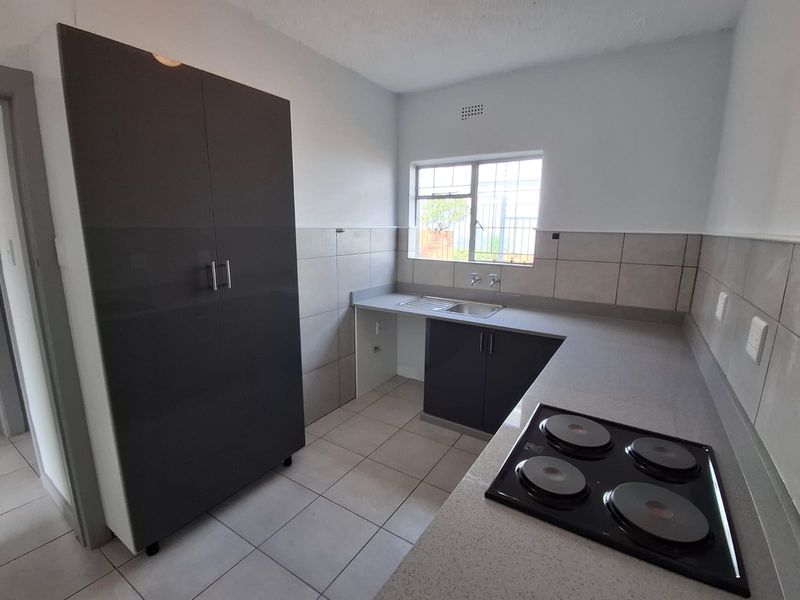 A clean, modern kitchen featuring dark grey cabinetry, a built-in electric hob, stainless steel sink, and neutral tiled finishes.