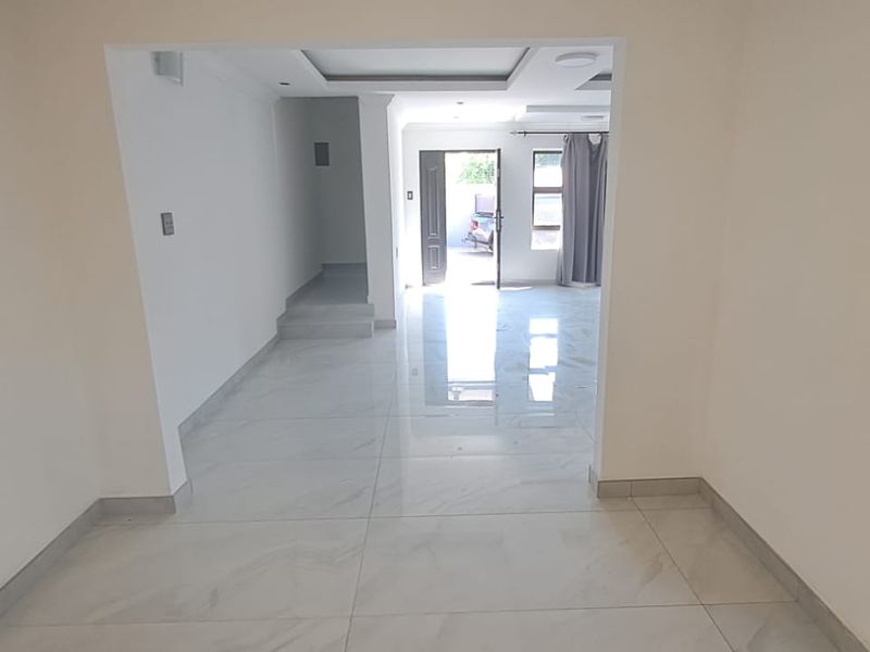 An open-plan living area featuring modern porcelain floor tiles, recessed ceiling lighting, and a drop ceiling design, leading towards the main entrance.