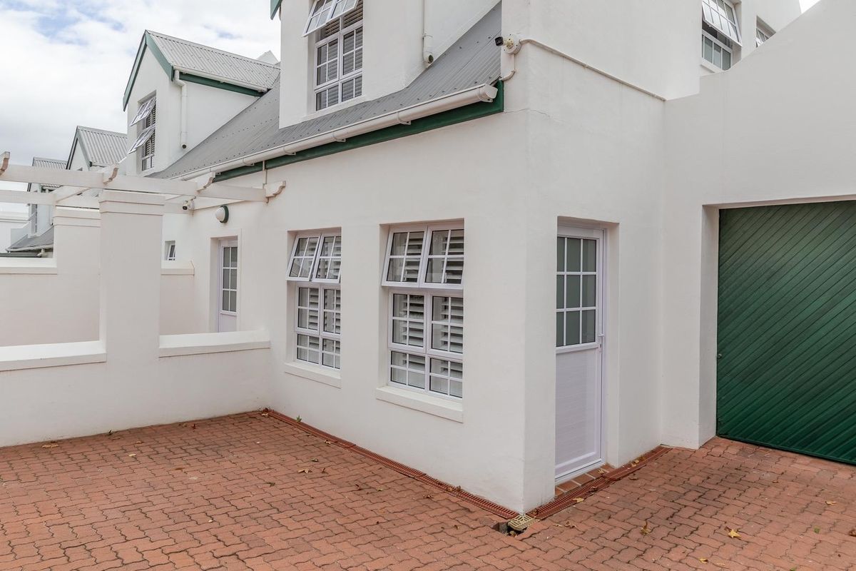 A well-maintained exterior rear view of the apartment featuring a paved courtyard, white facade, and a green garage door.