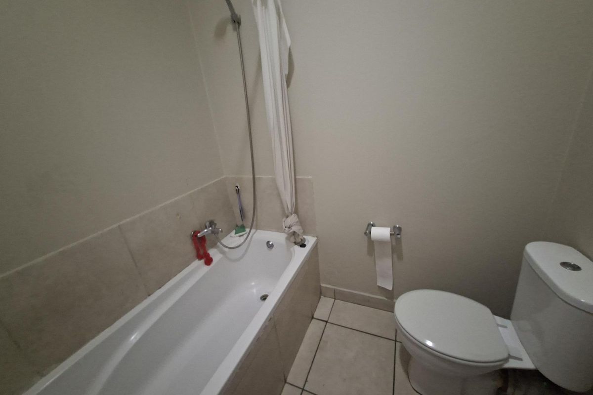 A functional bathroom featuring a standard bathtub with shower mixer and a toilet, finished with neutral wall paint and tiled flooring.