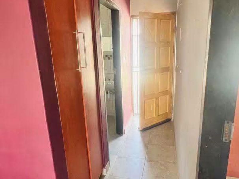 A functional hallway featuring tiled flooring and a built-in wooden cupboard, providing access to adjacent rooms.