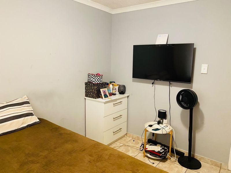 A bedroom featuring tiled flooring and a wall-mounted television setup, requiring minor cosmetic updates to the wall finishes.