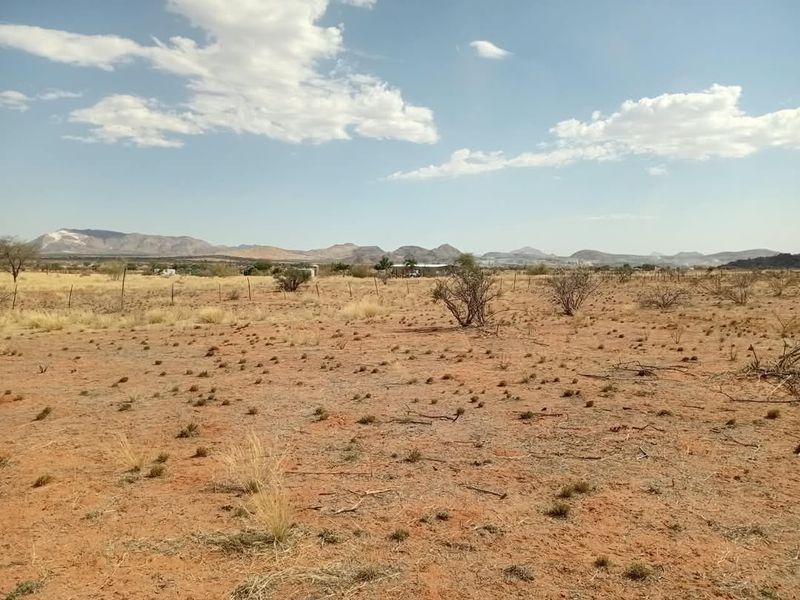 A wide-angle view of expansive, arid agricultural land featuring natural desert vegetation, wire fencing, and distant mountain ranges under a clear sky.